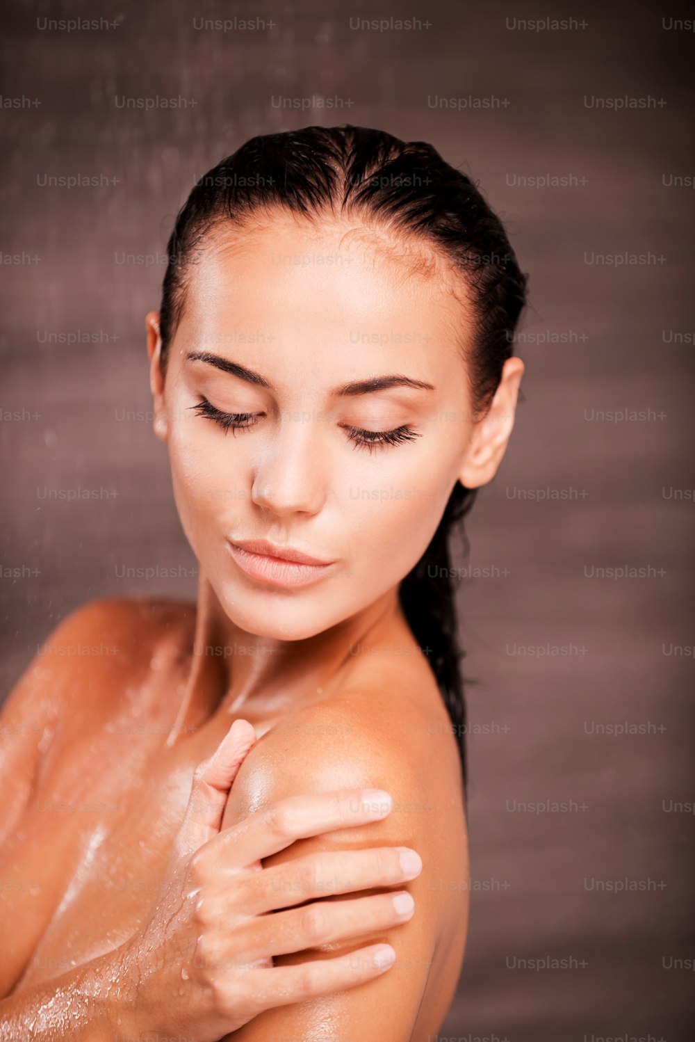 Bella giovane donna a torso nudo in piedi sotto la doccia e lavandosi la spalla