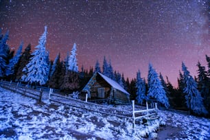 山の中のキャビン。幻想的な冬の流星雨と雪山。カルパチア、ウクライナ、ヨーロッパ。