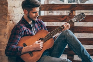 Hübscher junger Mann, der Gitarre spielt, während er auf der Fensterbank sitzt