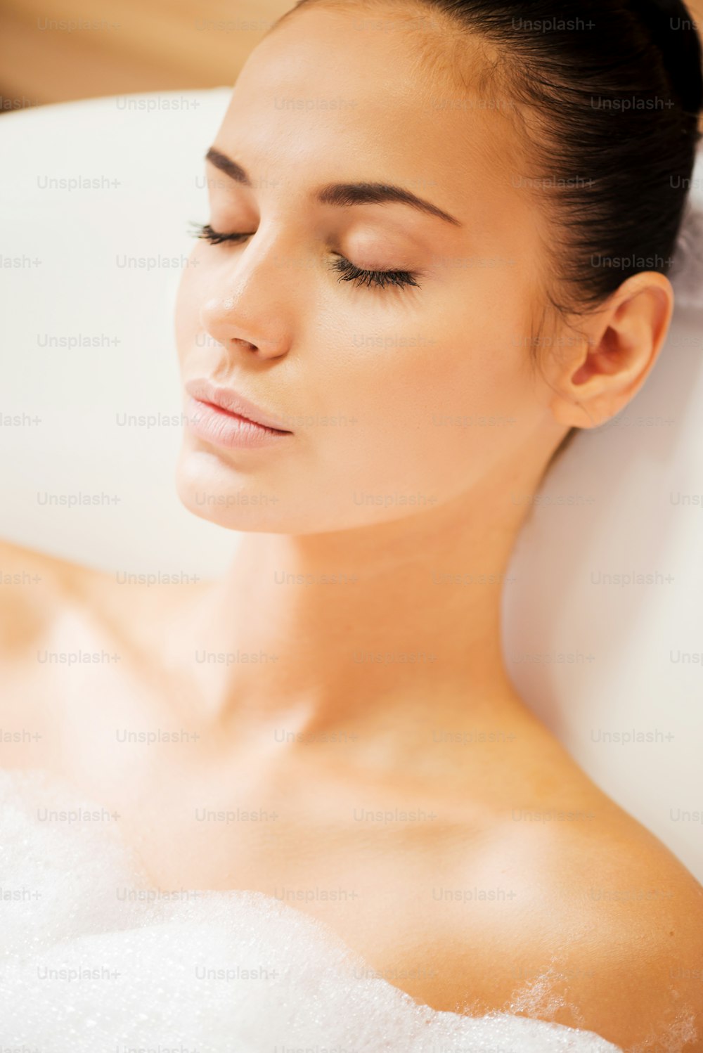 Top view of attractive young woman keeping eyes closed while enjoying luxurious bath