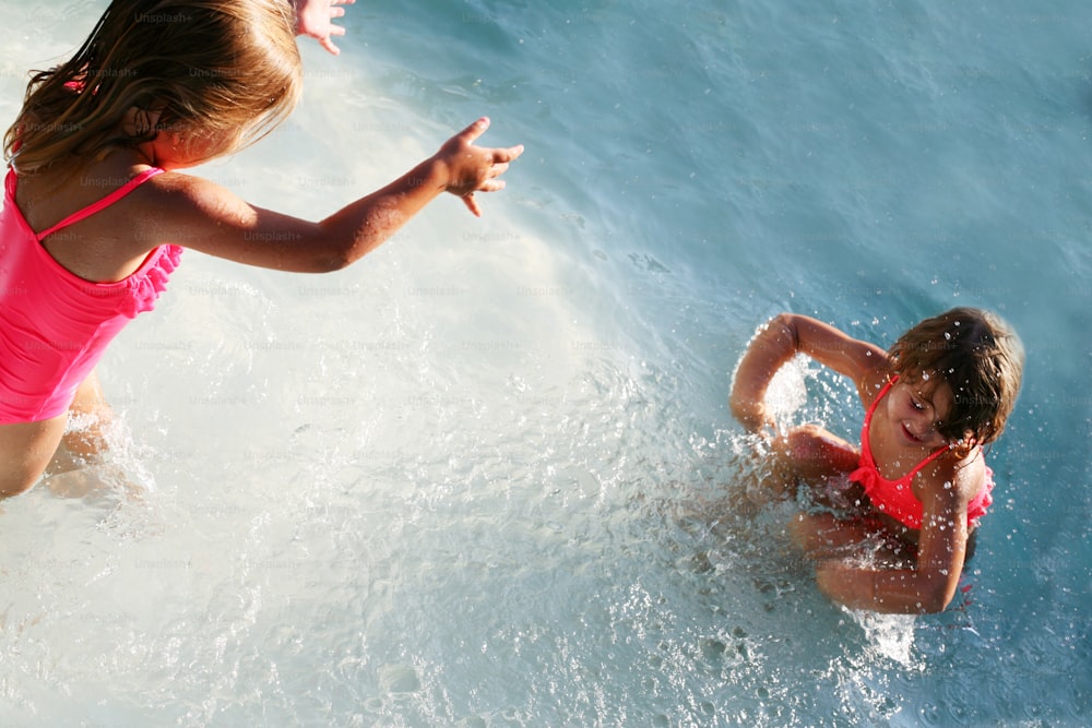 Two little girls having fun in the pool and splashes water everywhere.