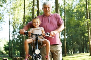 Senior man with granddaughter in bicycle basket, portrait.