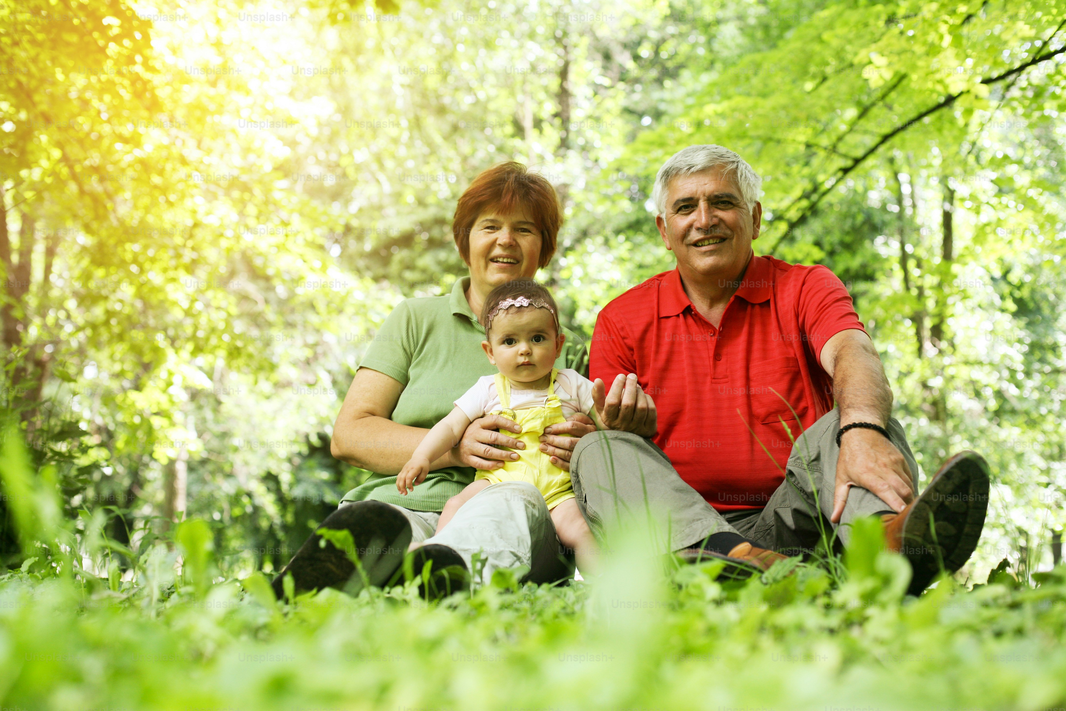 Foto Abuelos sentados en la hierba con una niña en el parque. Mirando a ...