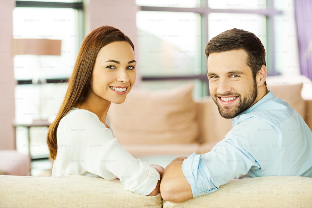 Vista trasera de una hermosa pareja joven que ama sentada junta en el sofá y sonriendo
