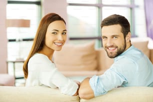 Rear view of beautiful young loving couple sitting together on the couch and smiling
