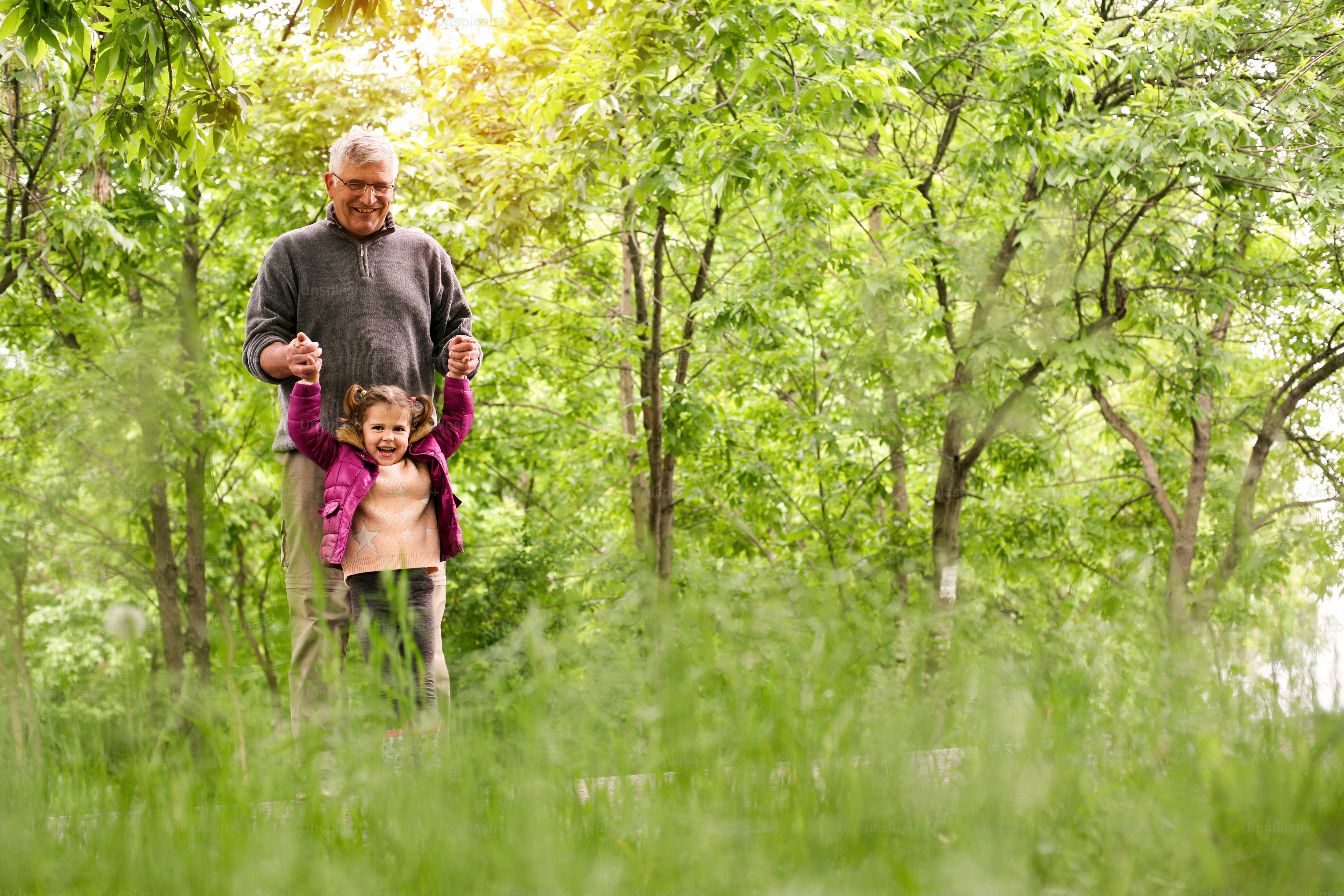 Happy kid playing with grandfather in the park.