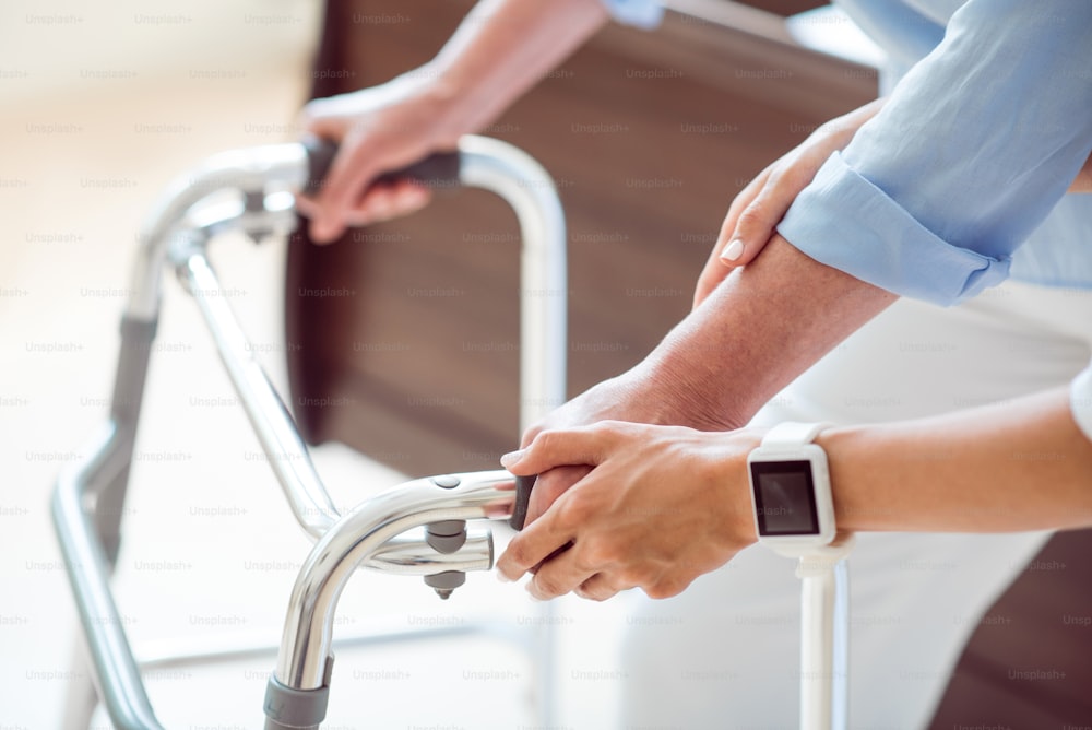 Medical help. Cropped image of professional doctor helping old woman with walking frame