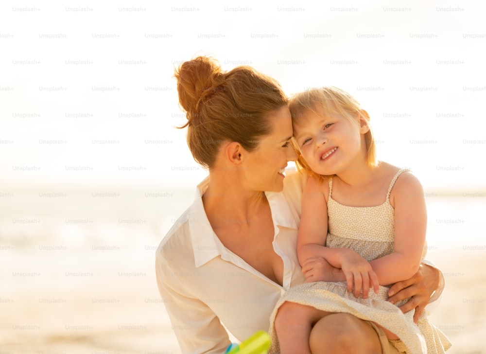 Porträt einer glücklichen Mutter und eines kleinen Mädchens am Strand am Abend
