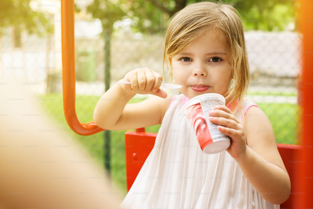 Cute and happy young girl eating ice cream outside.