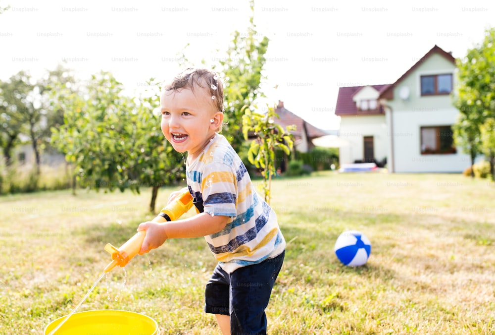 Little boy with water gun splashing somebody, fun in garden, sunny summer day, back yard