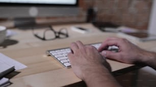 Unrecognizable man working from home, writing on computer keyboard, office desk