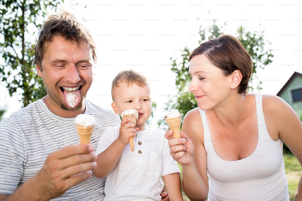 Young parents with their little son eating ice cream, sunny summer garden