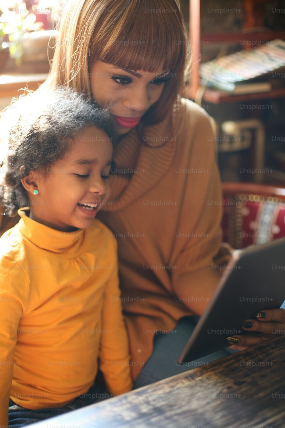 African mother with her smiling daughter using digital tablet at home.