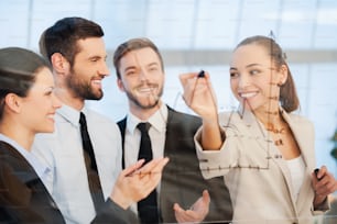Confident young businesswoman drawing a graph on glass and smiling while her colleagues standing near her