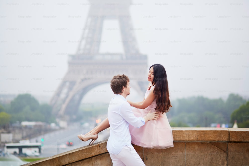 Beautiful romantic couple in love together near the Eiffel tower in Paris on a cloudy and foggy rainy day