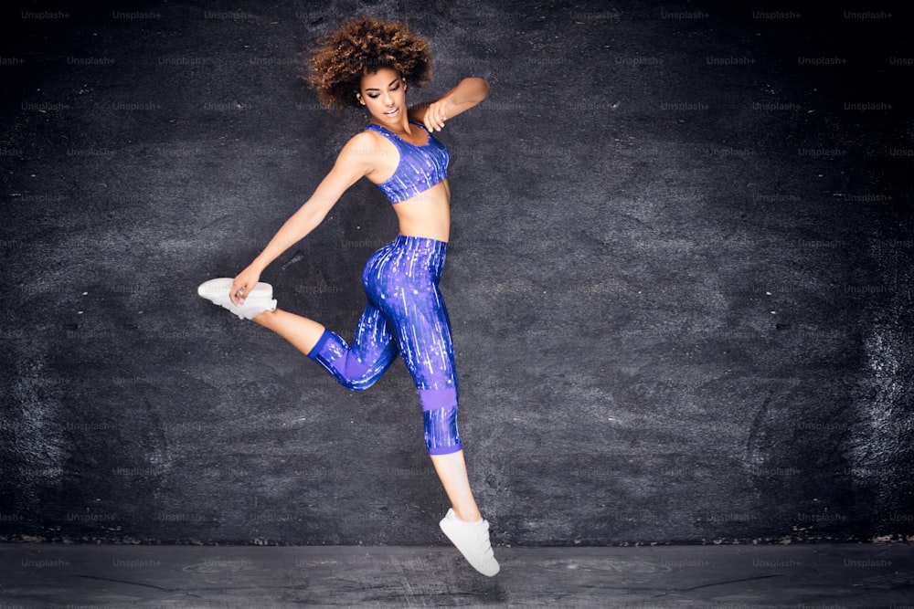 Menina afro-americana jovem dançando, pulando. Foto de estúdio. Corpo em forma. Felicidade.