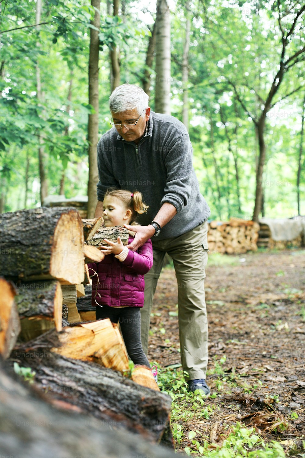 Little girl helping her grandfather to preparing tree trunks for winter season on the village.
