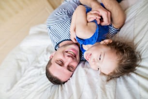 Young father having fun with his cute little daughter, lying in bed