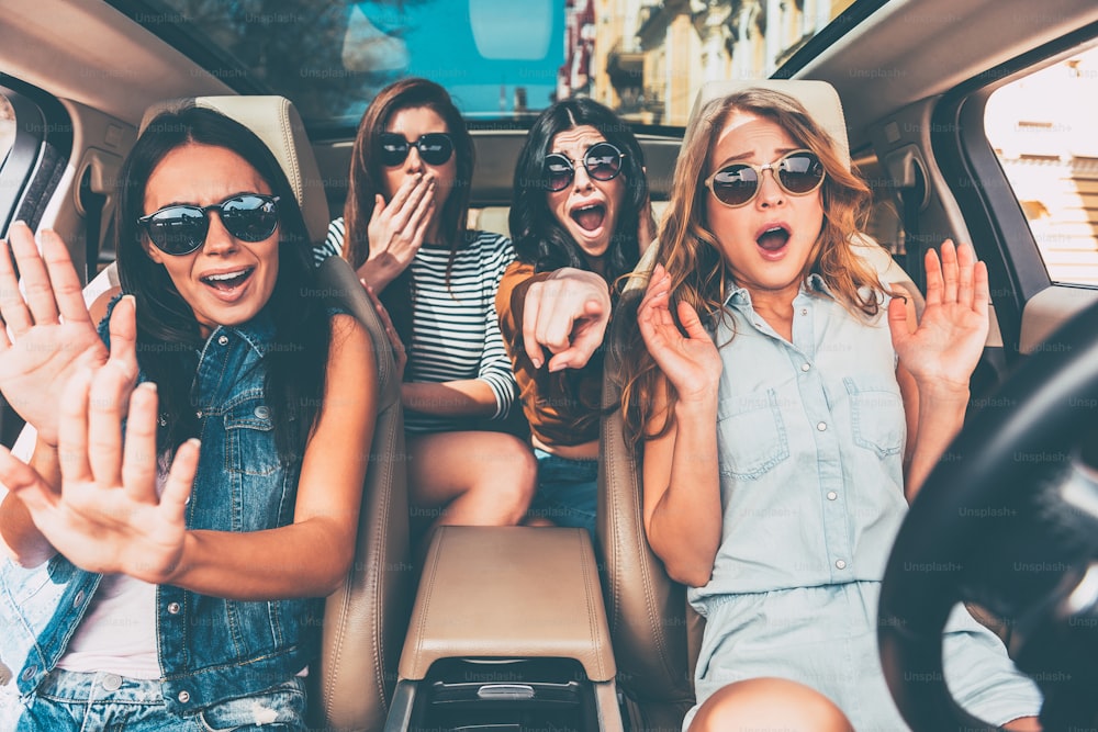 Four young women gesturing and looking terrified while sitting in car together