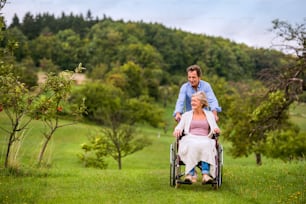 秋の緑の自然の中で車椅子に座る女性を押す年配の男性