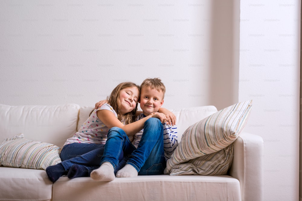 Cute little boy and girl sitting on a white couch. Studio shot, copy space