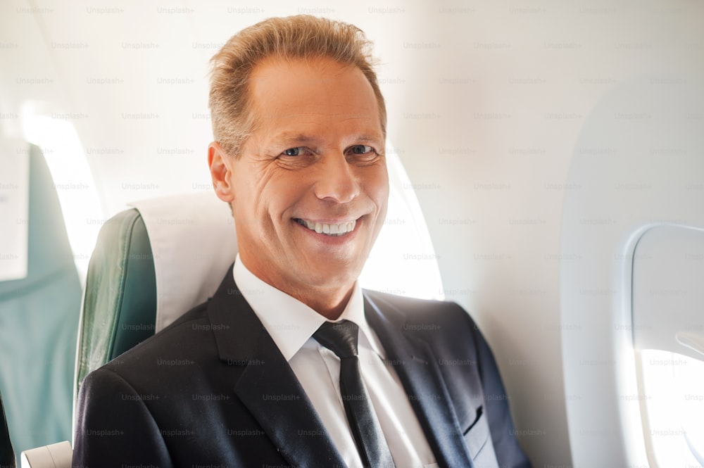 Confident mature businessman sitting at his seat in airplane and smiling