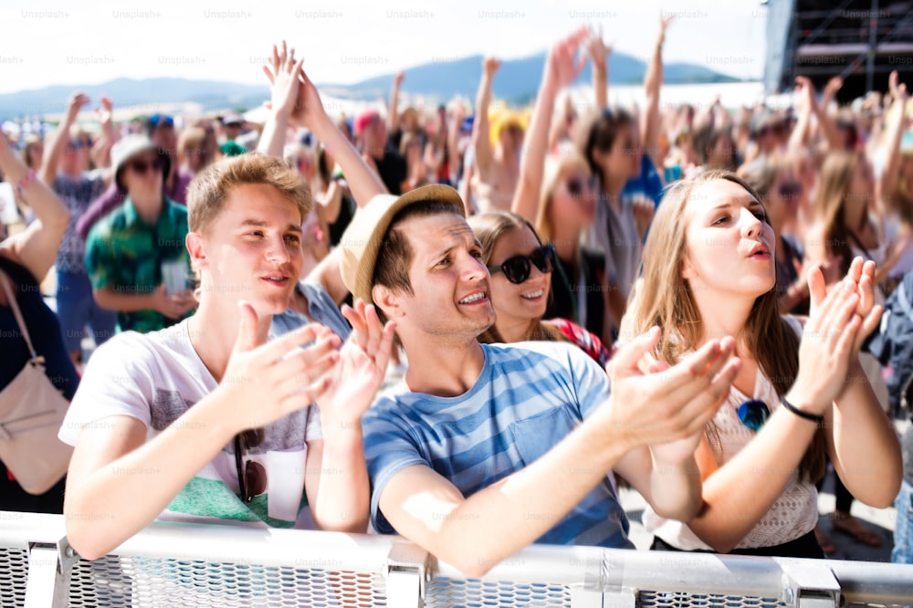 Adolescentes em festival de música de verão sob o palco em uma multidão se divertindo, batendo palmas, cantando
