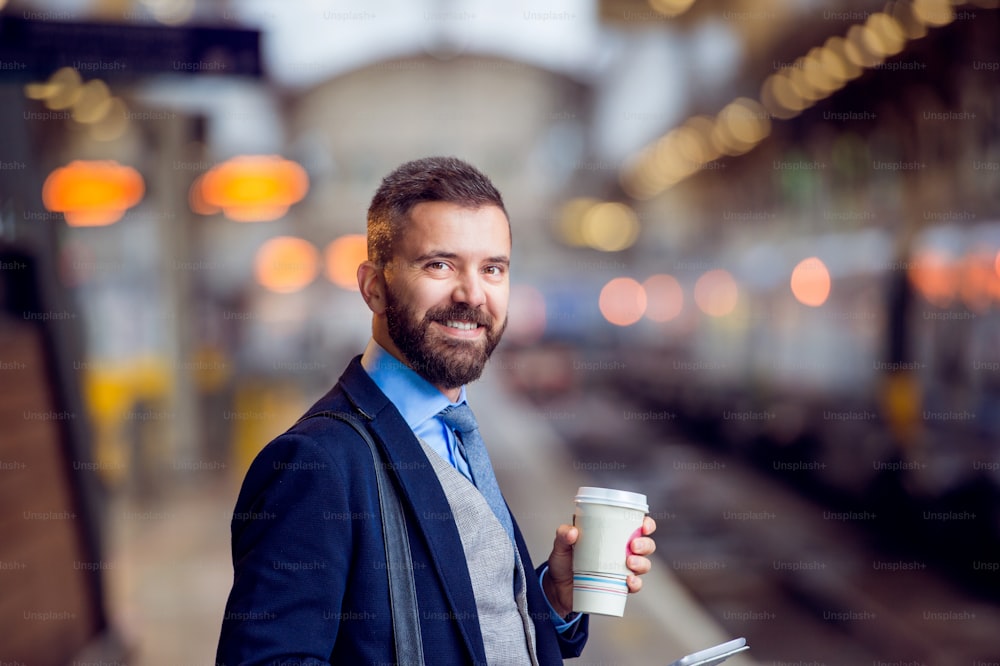 Hipster businessman holding a disposable coffee cup at the train station platform