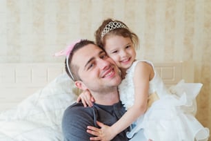 Cute little girl in princess dress with her father wearing crowns, smiling