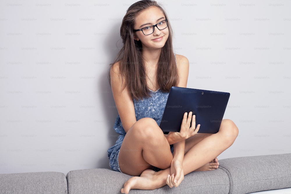 Young beautiful teenage girl sitting with tablet at home, learning. Smart girl with beautiful smile.