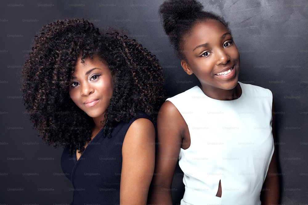 Zwei schöne afroamerikanische Mädchen lächeln und schauen in die Kamera. Schwestern posieren in eleganten Kleidern. Studioaufnahme.