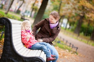 Beautiful mother and daughter sitting on a bench by fall