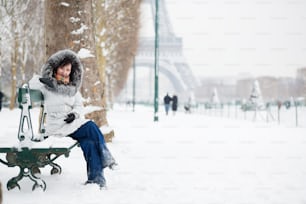 Belle fille à capuche de fourrure assise sur un banc près de la tour Eiffel