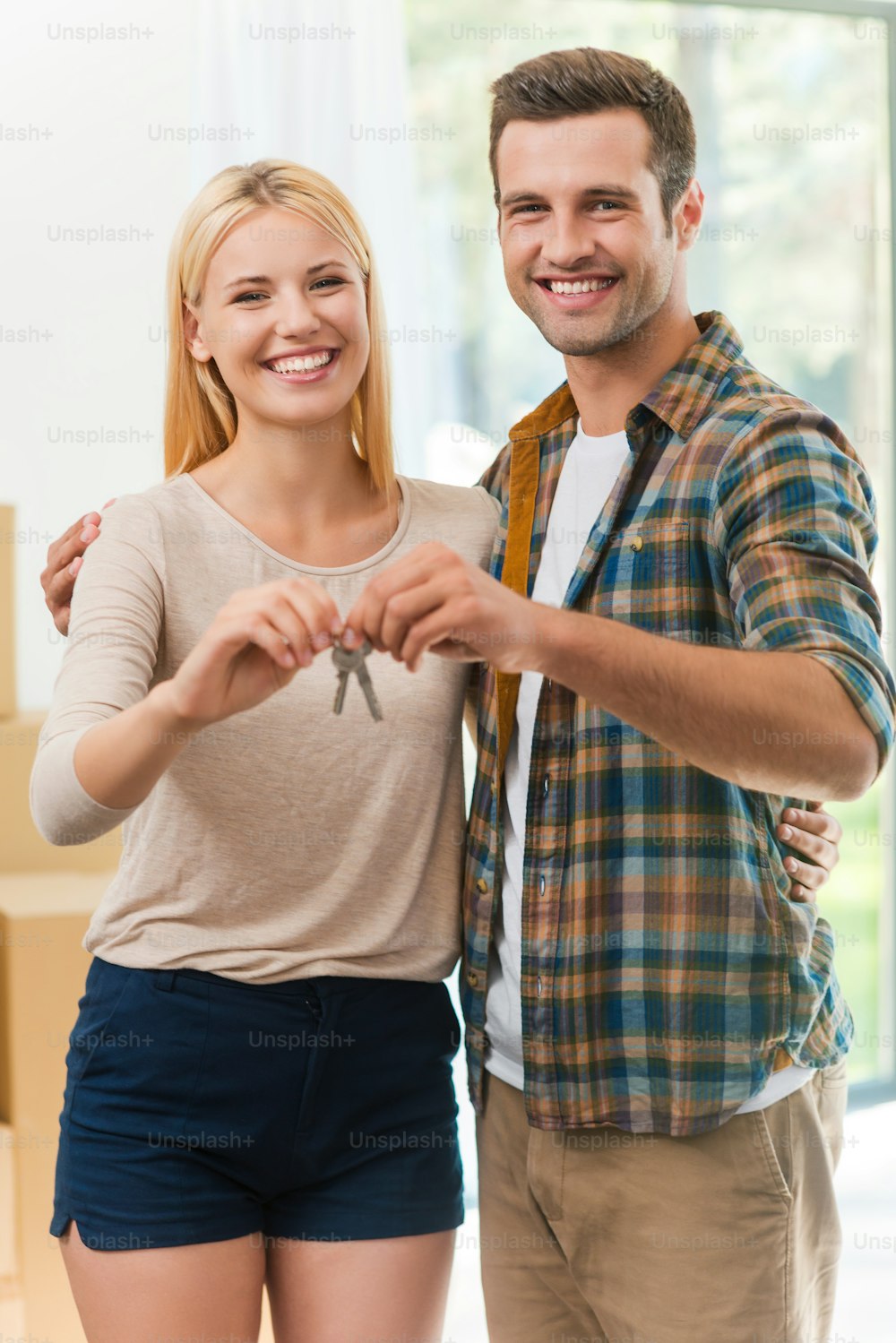Beautiful young loving couple holding keys and smiling while standing in their new house