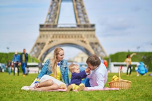 Glückliche dreiköpfige Familie, Mutter, Vater und kleiner kleiner Junge, beim Picknick in Paris in der Nähe des Eiffelturms