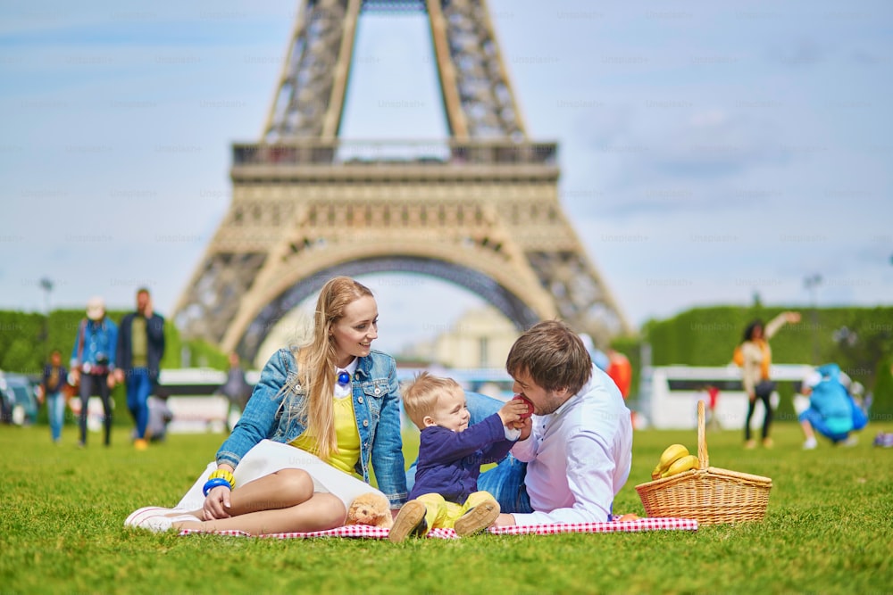 Feliz familia de tres, madre, padre y niño pequeño, haciendo un picnic en París cerca de la torre Eiffel