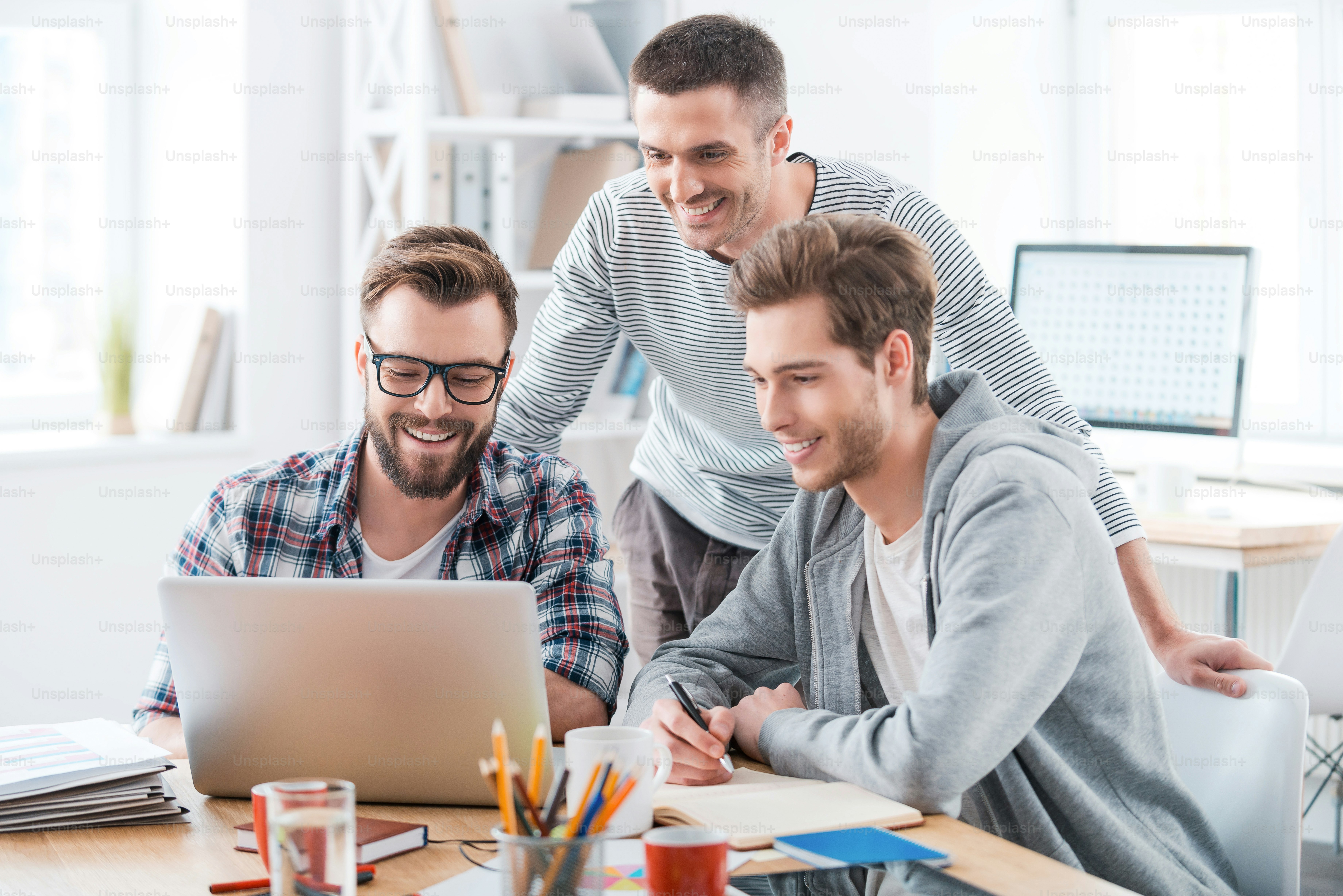 Three cheerful young men working together while sitting at their working place in office