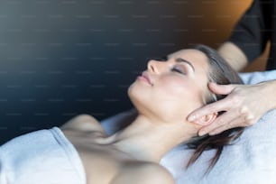 Massaggiatore che tratta il viso di una bella giovane donna sdraiata sul lettino da massaggio