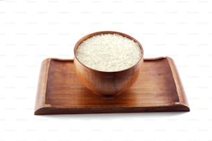 Ein Bild einer Holzschüssel mit ungekochtem Reis, auf einem passenden Holztablett platziert.