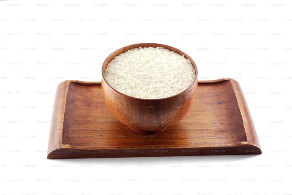 A picture of a wooden bowl of uncooked rice, placed on a matching wooden tray.