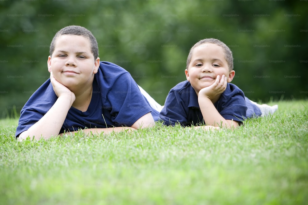 two young boys laying in the grass with their hands on their chins