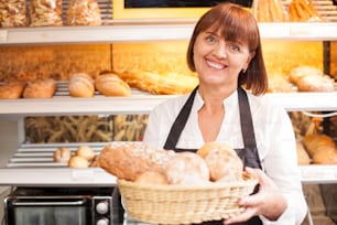 Beautiful saleswoman is standing in bakery. She is holding a basket of pastry and smiling