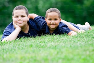 two young boys laying in the grass with their arms around each other