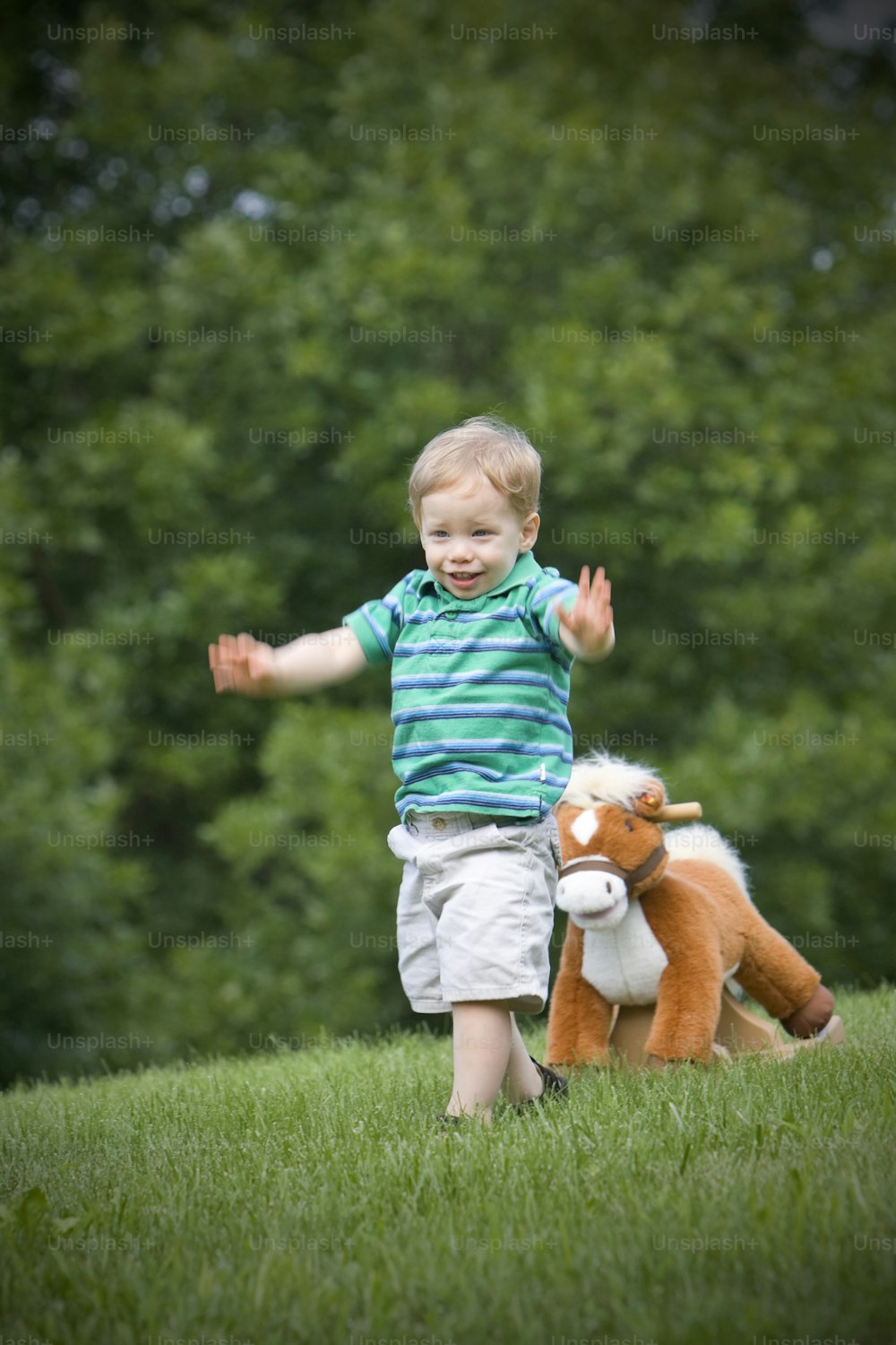 a little boy that is standing in the grass with a stuffed animal