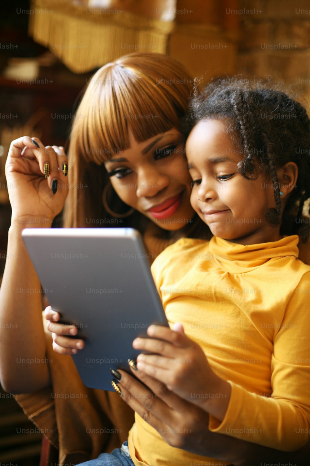 Mère africaine avec sa fille souriante à l’aide d’une tablette numérique à la maison.