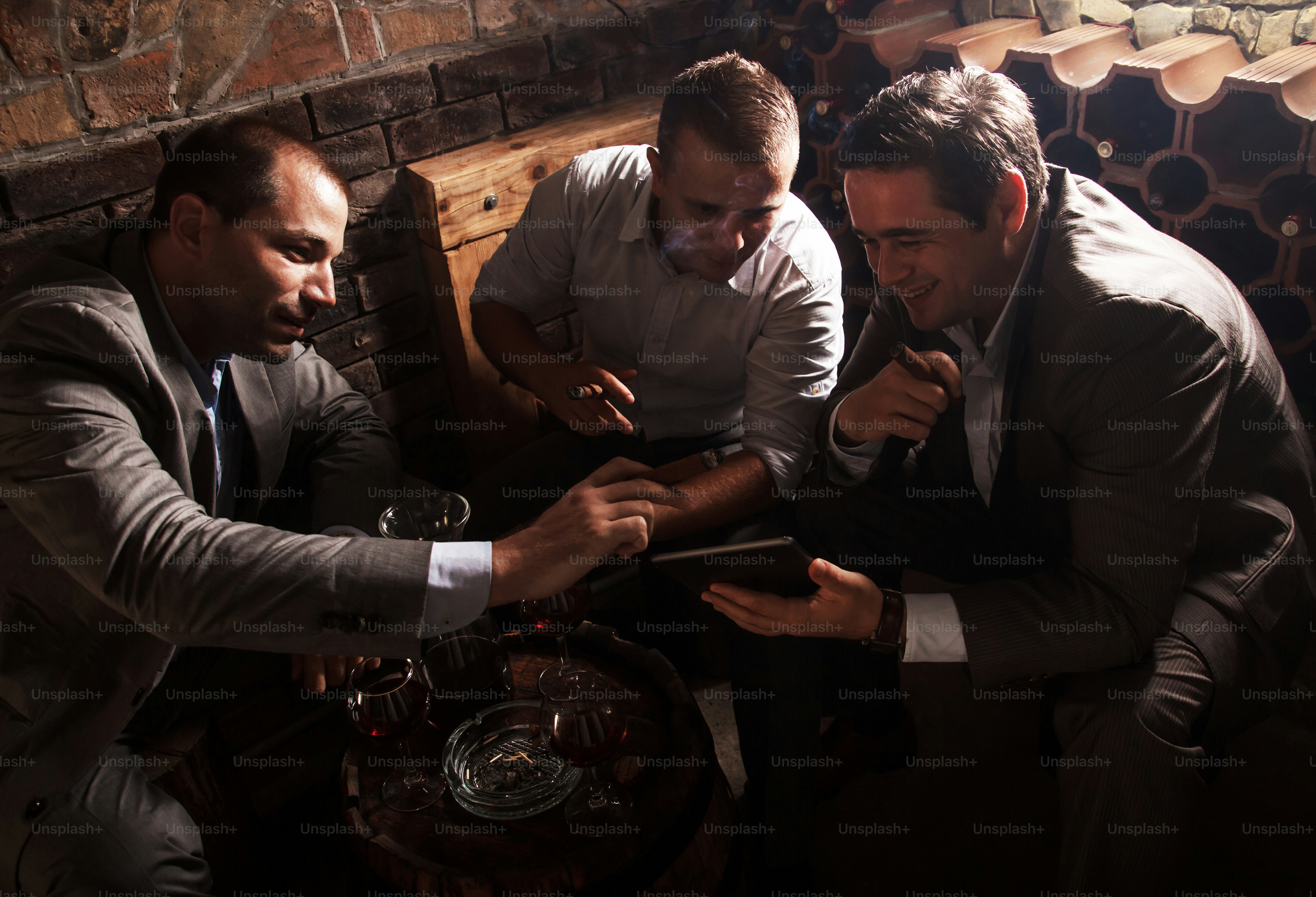 와인 저장고에 앉아 와인을 마시고 시가를 피우는 세 명의 사업가가 직장에서 힘든 하루를 보낸 후 휴식을 취하고 있습니다.