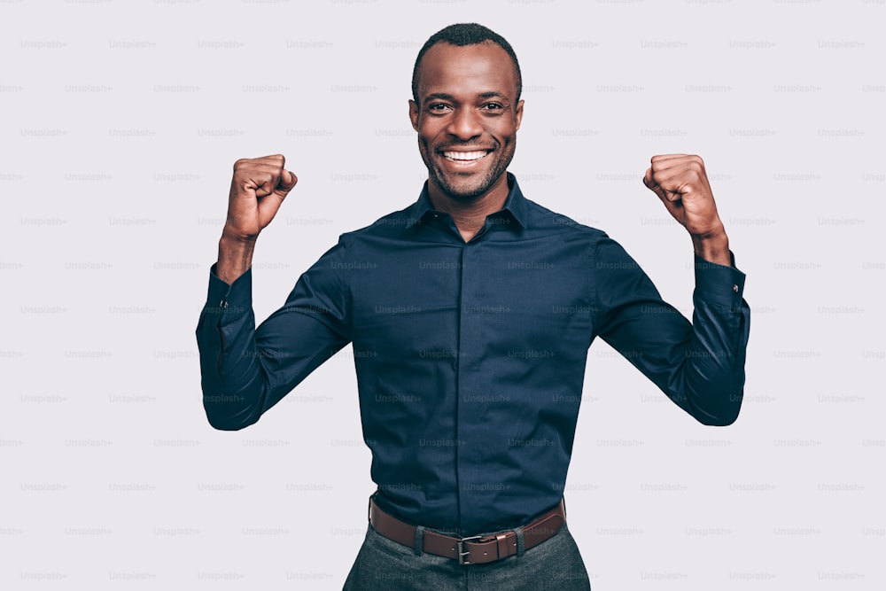 Happy young African man gesturing and looking at camera with smile while standing against grey background
