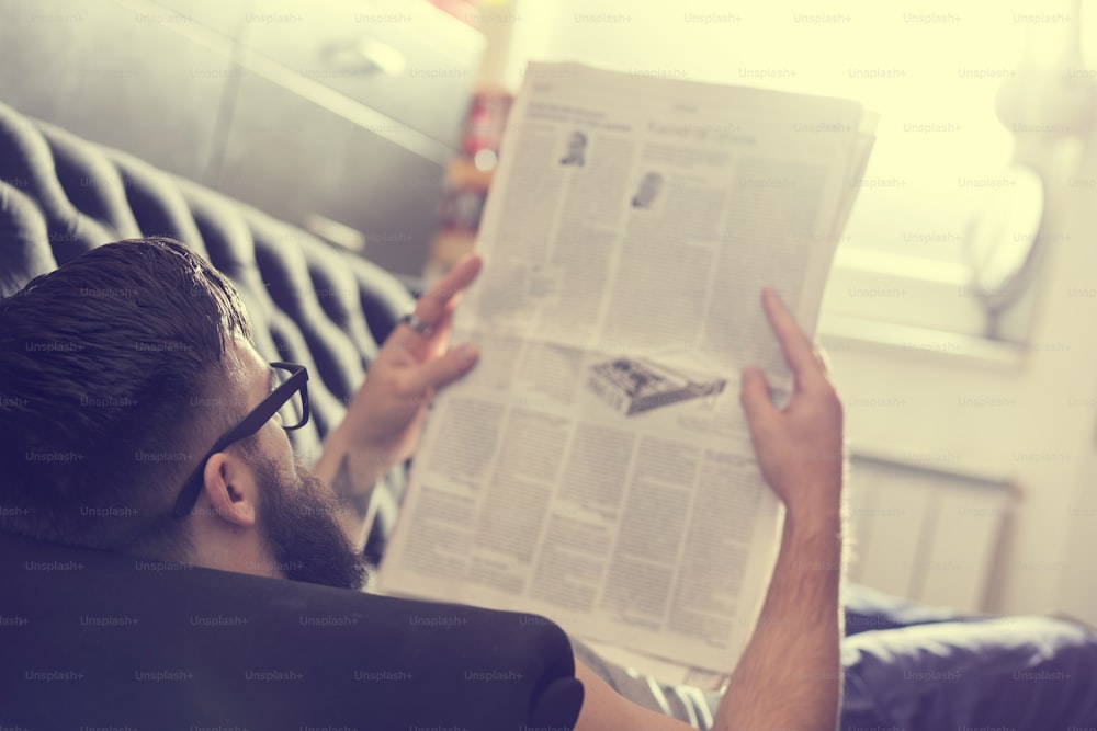 Modelo masculino acostado en un sofá en una sala de estar, leyendo periódicos