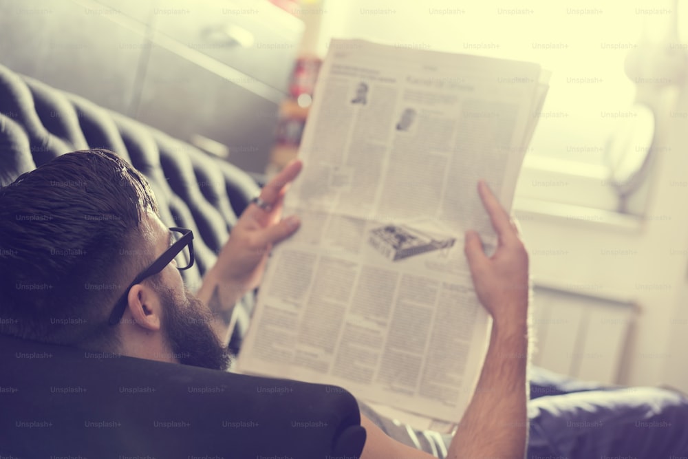 Male model lyingon a couch in a living room, reading newspapers