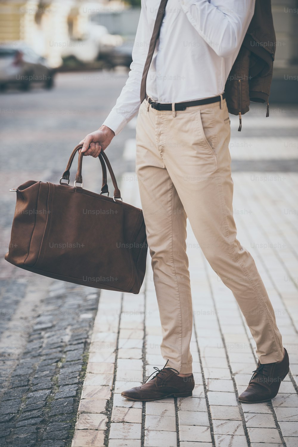Part of man holding leather bag while walking outdoors